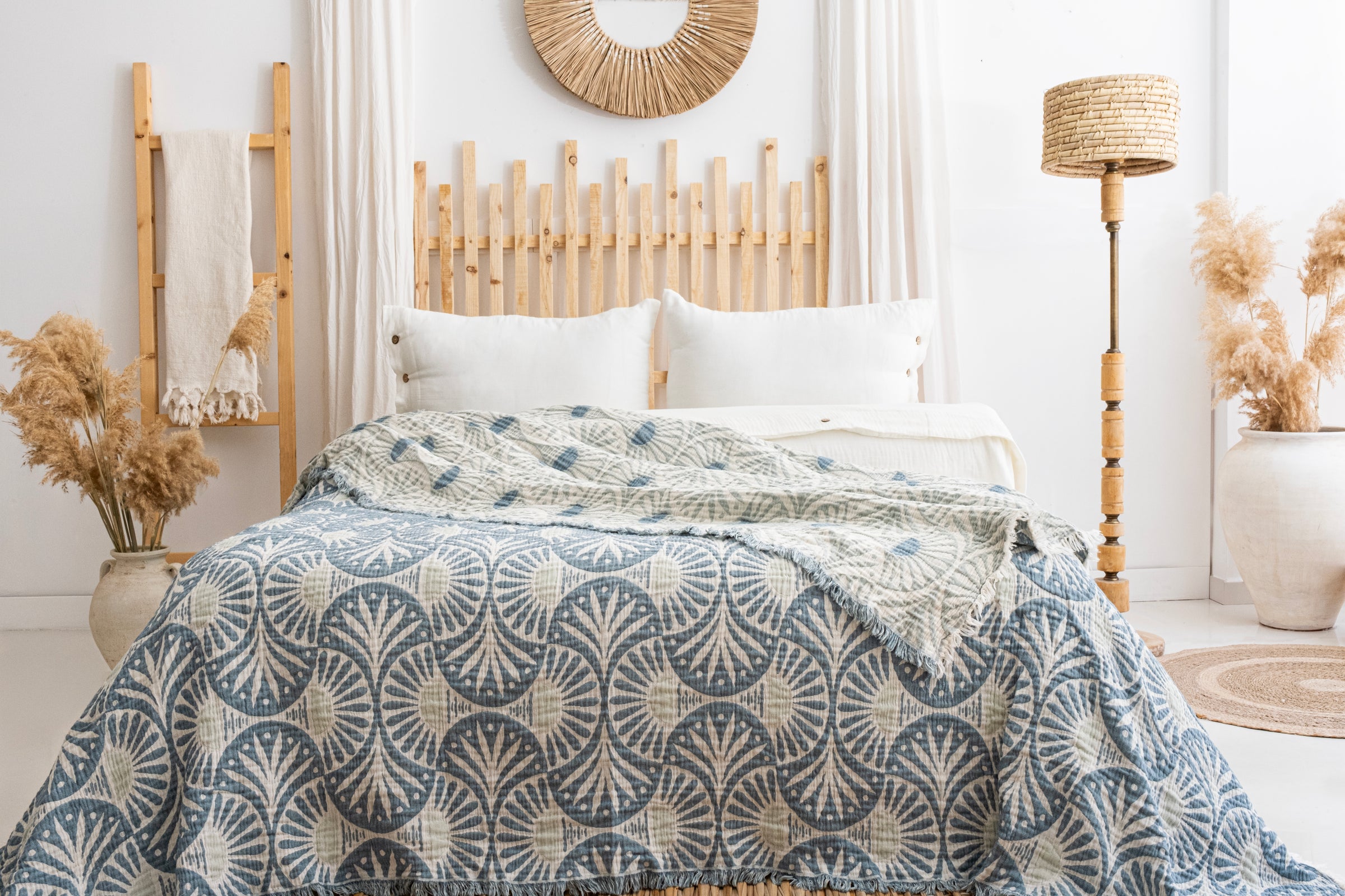 A cozy bedroom with a wooden headboard, white pillows, and the Gingko Muslin Bed Blanket – Teal (King-Oversized Queen) by turkanhome.com. Woven accents, pampas grass, and neutral decor create a calm, airy atmosphere.