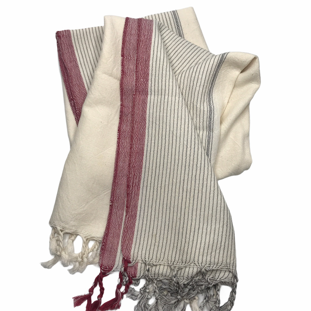 The Ivory Colorblock Peshtemal by turkanhome.com is a hand loomed cotton bath towel featuring thin black stripes, red vertical bands, and fringed edges, shown folded on a white background.