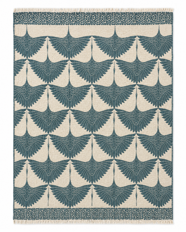The Crane Muslin Throw Blanket Natural Border– Reversible Turkish Cotton from turkanhome.com features a rectangular design with a repeating pattern of teal birds in flight on a cream background, framed by a row of circular floral motifs and finished with fringe on the shorter edges—this elegant piece combines the beauty of Turkish cotton with reversible versatility, offering both style and comfort to your home.