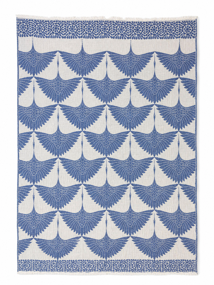 Crafted from soft Turkish muslin cotton, the Crane Muslin Throw Blanket Natural Border from turkanhome.com features a repeating blue crane design on a white background, with rows of spread-wing cranes and a decorative floral border at the top. This reversible Turkish cotton throw combines style and comfort, making it an ideal accent for your home.