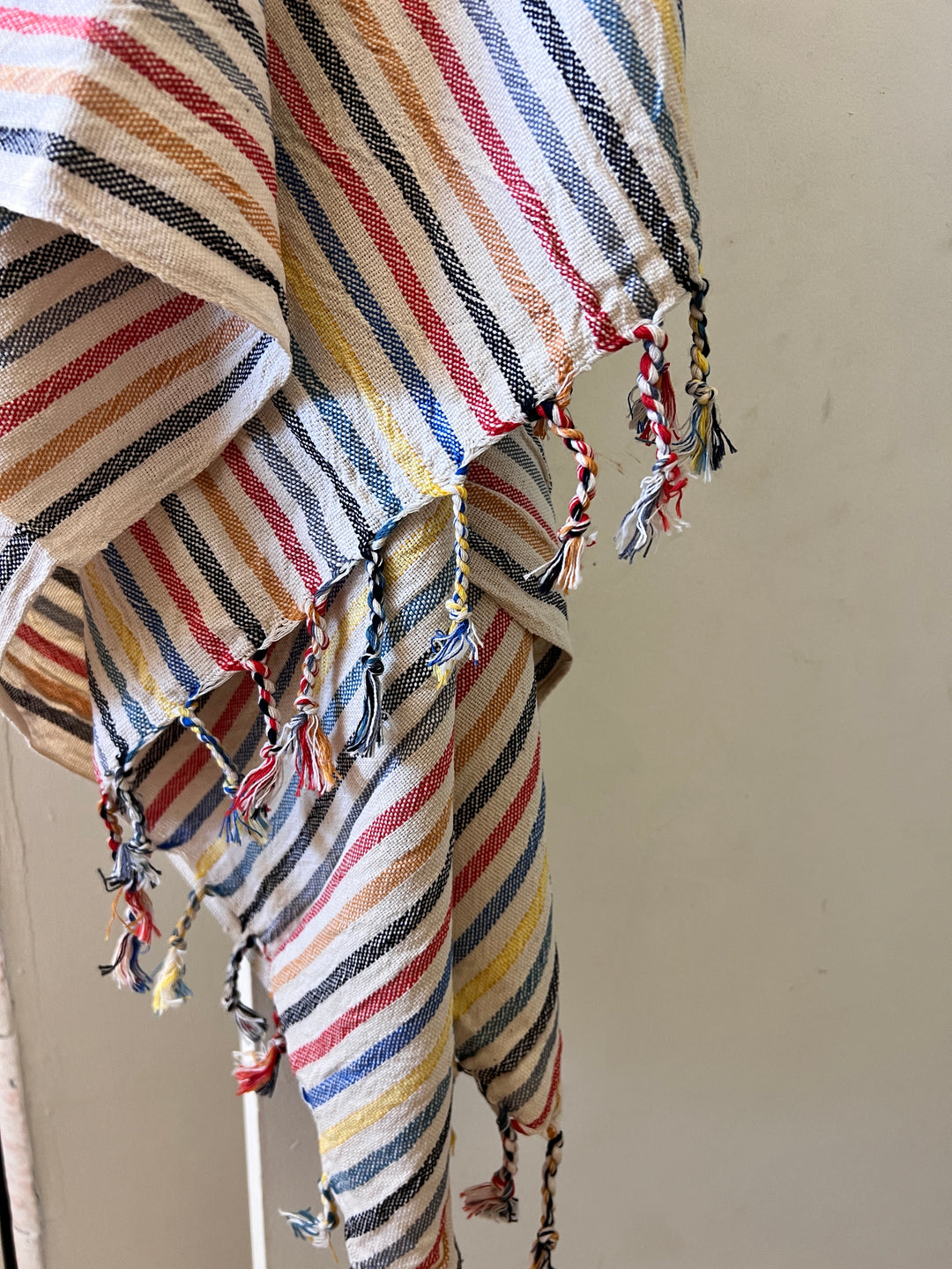 A close-up of the Mardin Handwoven Turkish Towel by turkanhome.com, featuring diagonal red, yellow, blue, and black stripes on white with twisted multicolor fringed edges—perfect as a throw or shawl.