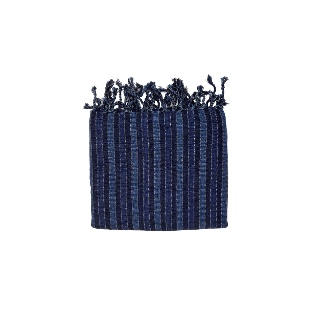 The Black Sea Handwoven Turkish Towel from turkanhome.com is crafted from all-natural fibers and features navy blue stripes, light blue vertical lines, and fringed edges. It can be used as a towel, throw, or shawl.