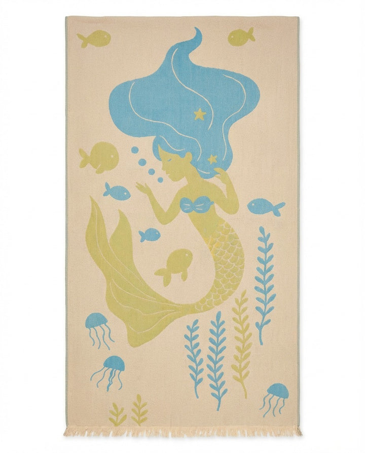 The Mermaid Turkish Towel by turkanhome.com is a beige, 100% cotton, reversible beach towel featuring a blue-haired mermaid with a green tail and playful sea creatures in a whimsical style. Quick drying and perfect for the beach.