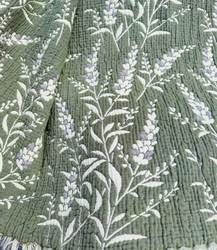 Experience year-round comfort and elegance with the 7-Layer Cotton Muslin Quilted Blanket - Lavender Field from turkanhome.com. This all-season bedspread showcases a textured green quilted surface accented by delicate white and light purple lavender floral patterns, blending style and coziness for any time of the year.