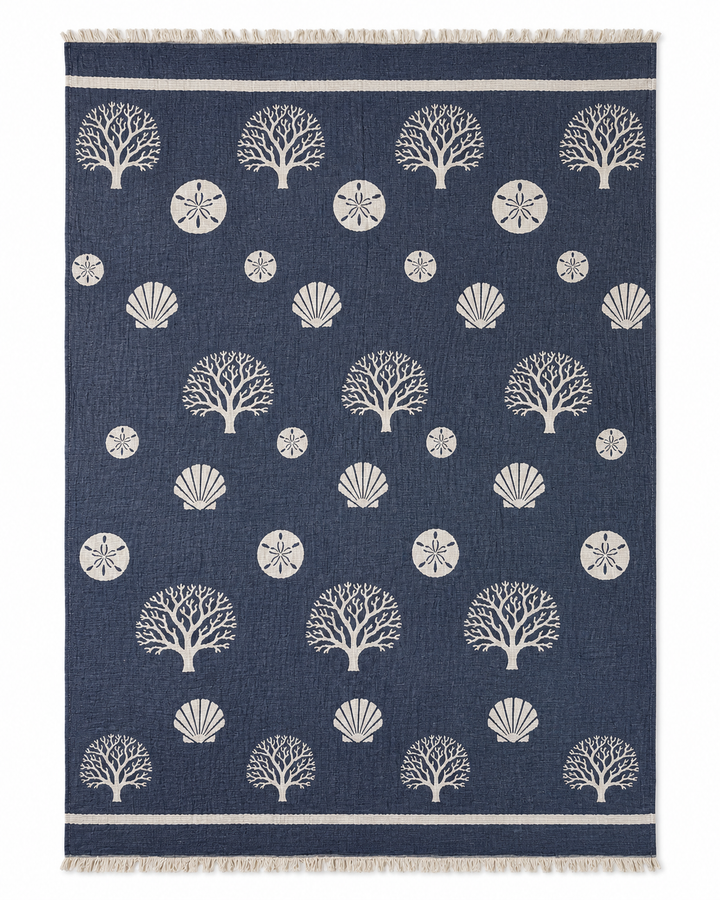 Introducing the Coastal Muslin Throw Blanket – Reversible Turkish Cotton from turkanhome.com: a navy blue throw featuring an elegant pattern of white coral, seashells, and sand dollars, finished with slim white stripes and fringe along the short edges—ideal as a beach blanket or stylish coastal accent for effortless seaside charm.