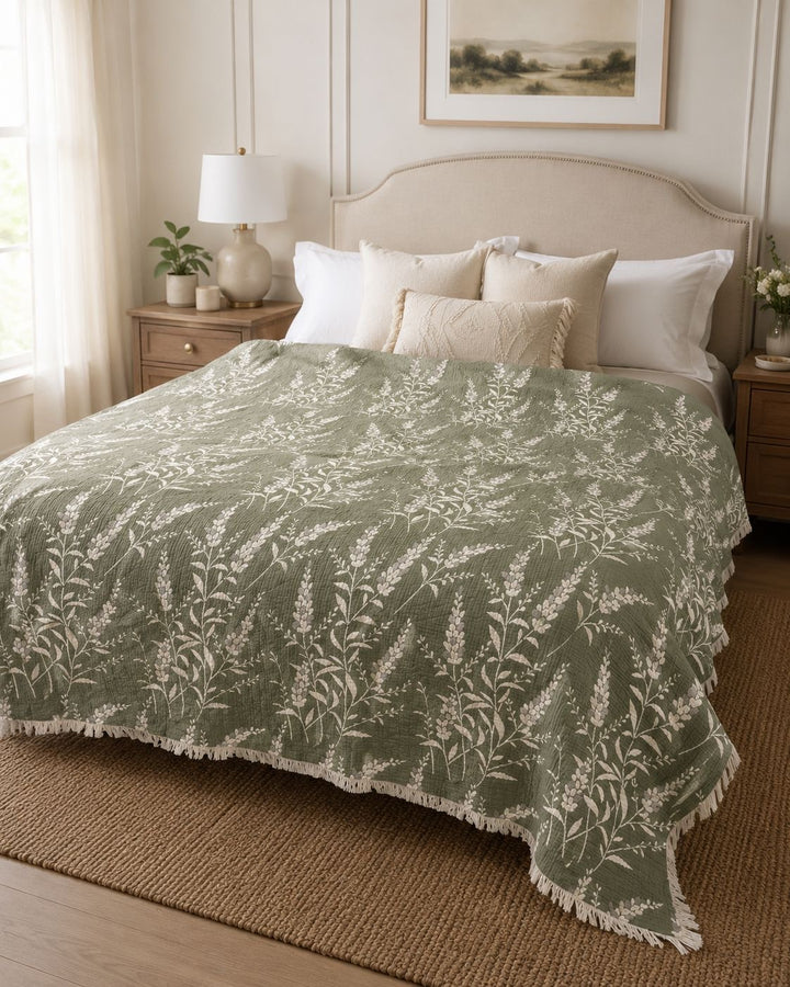 A neatly made bed featuring the 7-Layer Cotton Muslin Quilted Blanket in Lavender Field from turkanhome.com, adorned with cream pillows, sits between two wooden nightstands in a bright, cozy bedroom with neutral decor.