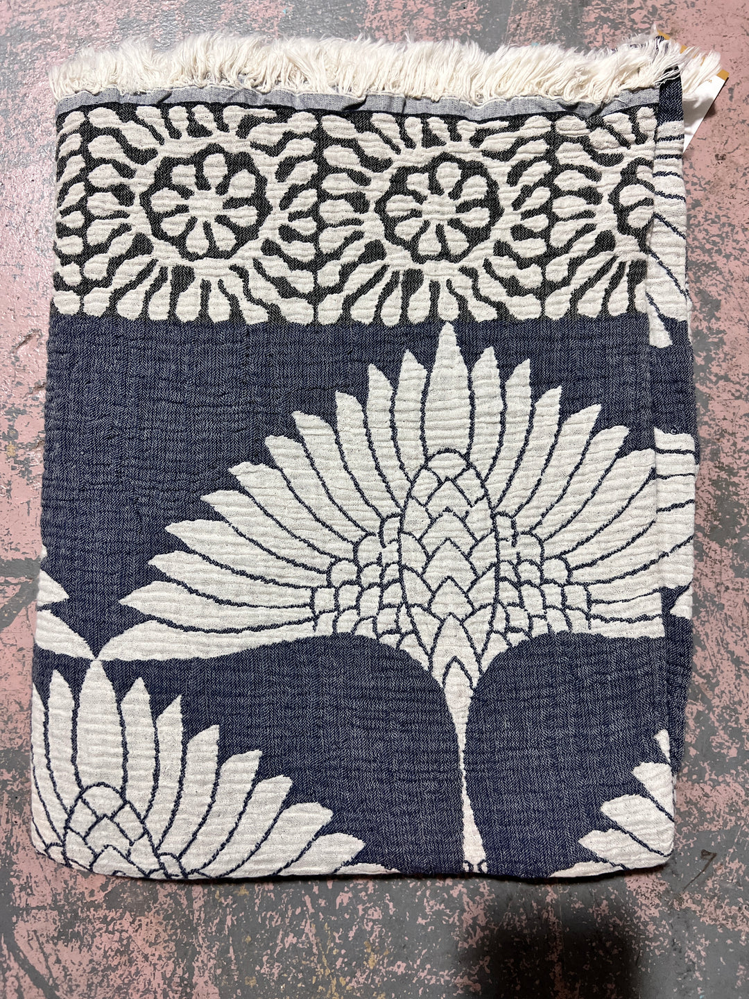 The Crane Muslin Throw Blanket by turkanhome.com is a reversible Turkish cotton throw with a navy and white floral design, showcasing a large central flower, smaller flowers on top, and a fringed border.