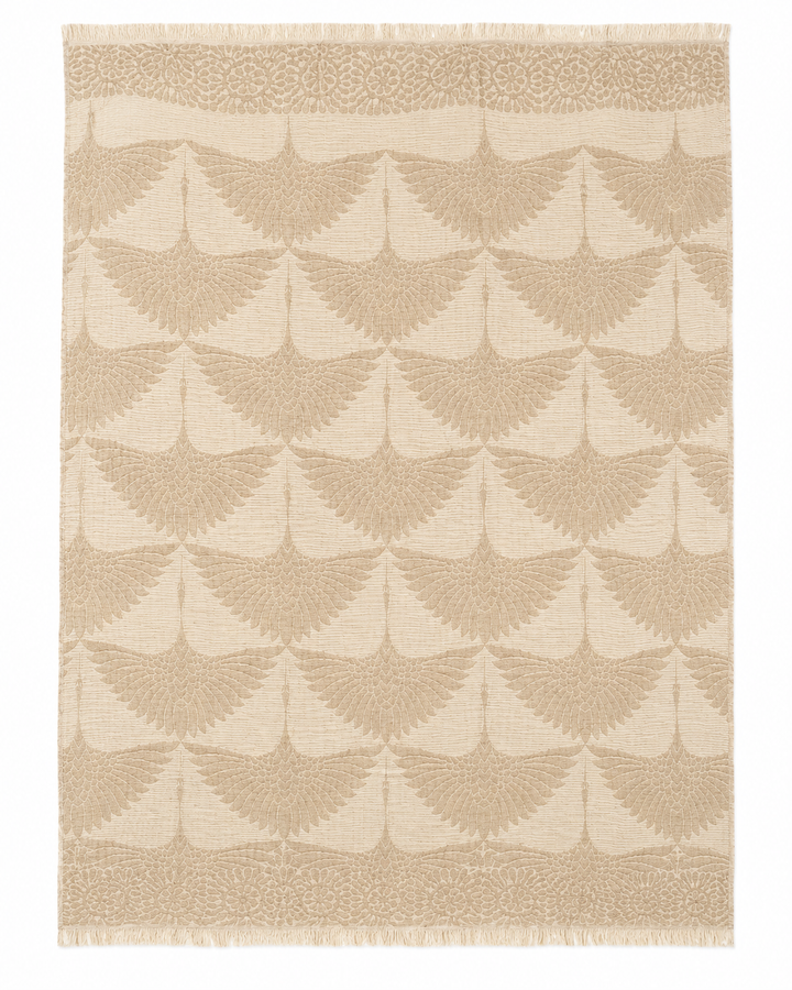 Experience the Crane Muslin Throw Blanket from turkanhome.com—a reversible Turkish cotton throw in natural tones, featuring a beige and light brown palette with repeating fan-shaped, scalloped patterns. Reminiscent of an area rug, it boasts a soft woven texture, a decorative border along the shorter edges, and subtle fringe at the top and bottom for added elegance.