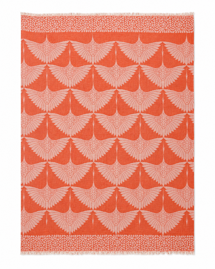 Crafted from luxurious Turkish muslin cotton, the Crane Muslin Throw Blanket Natural Border–Reversible Turkish Cotton by turkanhome.com features a square design adorned with a repeating pattern of stylized light pink birds with outstretched wings on an orange background, framed by an elegant floral border. This throw blanket combines comfort and sophistication for any setting.