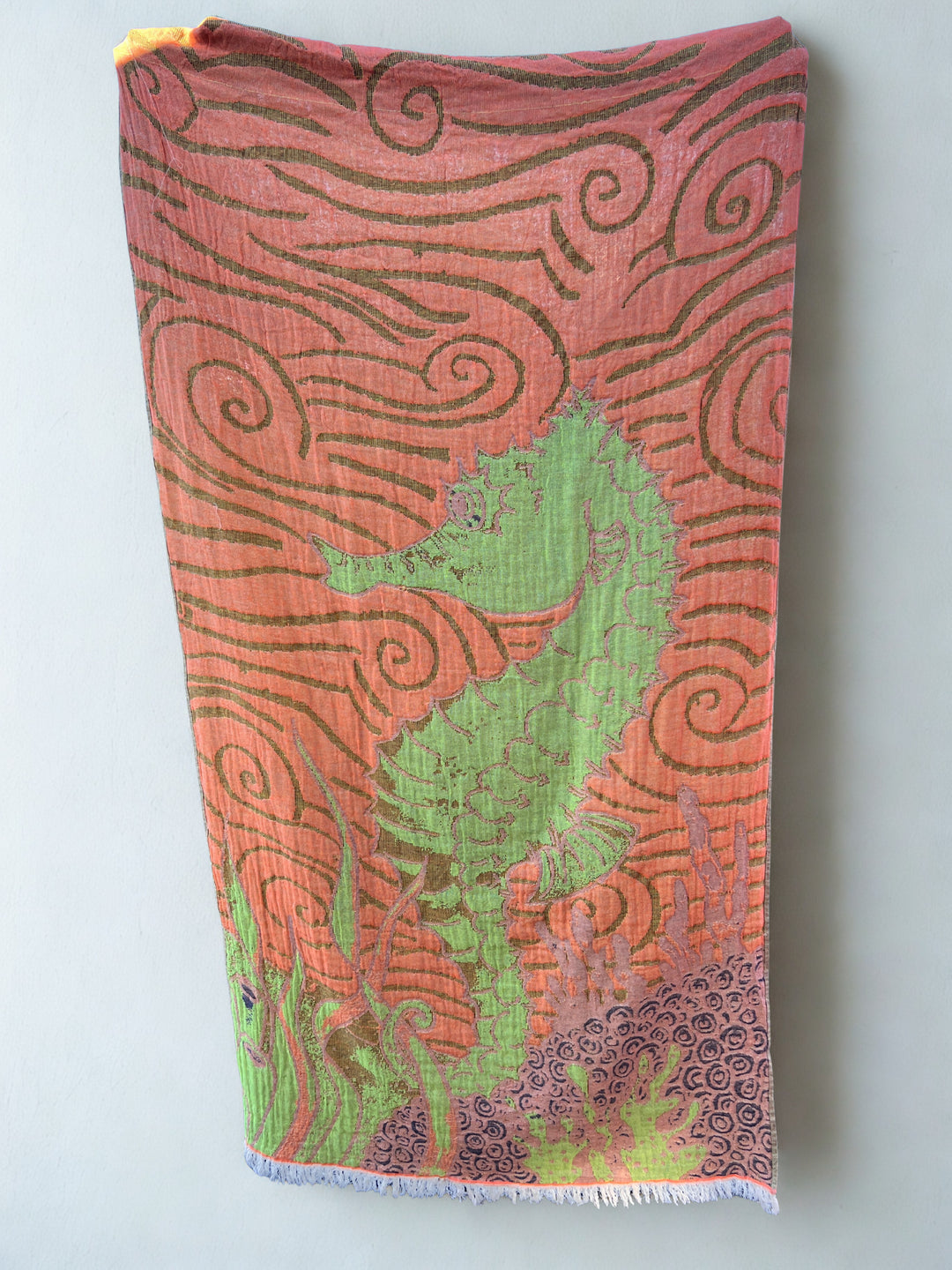 The Seahorse Turkish Towel – Quick Drying Towel by turkanhome.com features a bold green seahorse with swirling orange and purple patterns and seaweed-like designs, shown draped flat against a light gray wall.