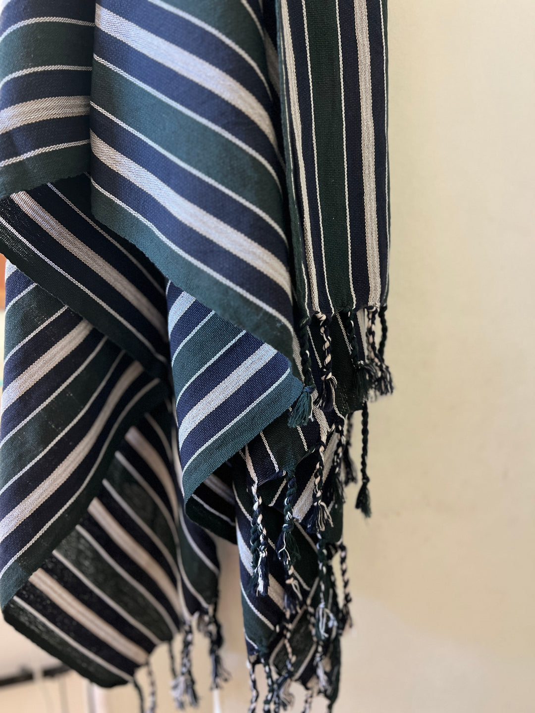 A close-up of the Halep Handwoven Turkish Towel by turkanhome.com, handcrafted from all-natural fibers, with white and light blue vertical stripes and fringed tassels—classic Turkish towel design.