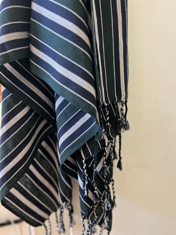 A close-up of the Halep Handwoven Turkish Towel by turkanhome.com, handcrafted from all-natural fibers, with white and light blue vertical stripes and fringed tassels—classic Turkish towel design.