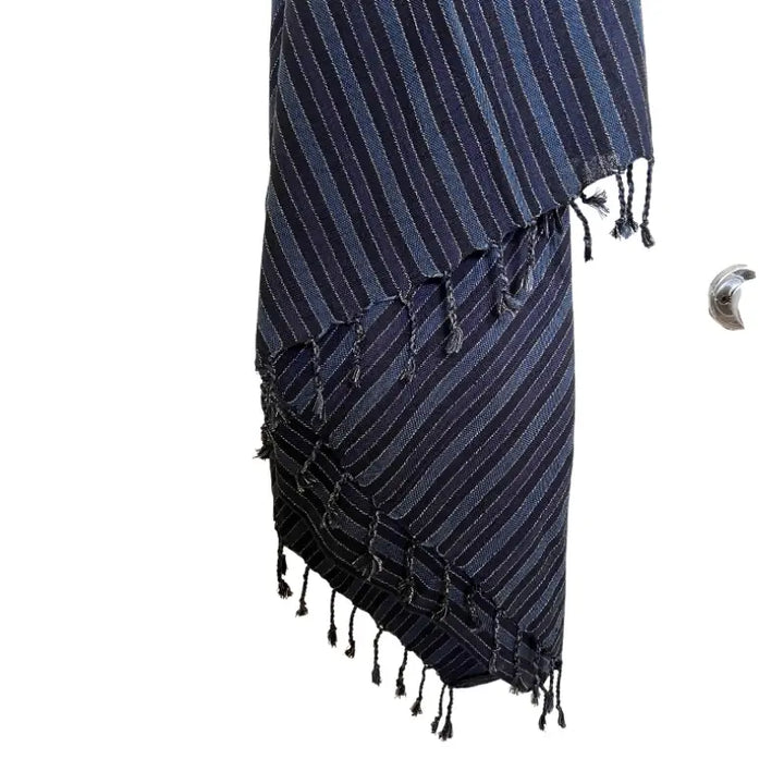 The Black Sea Handwoven Turkish Towel, Throw, Shawl by turkanhome.com features dark blue artisan-made fabric with thin, light stripes and fringed edges, displayed against a plain white background.
