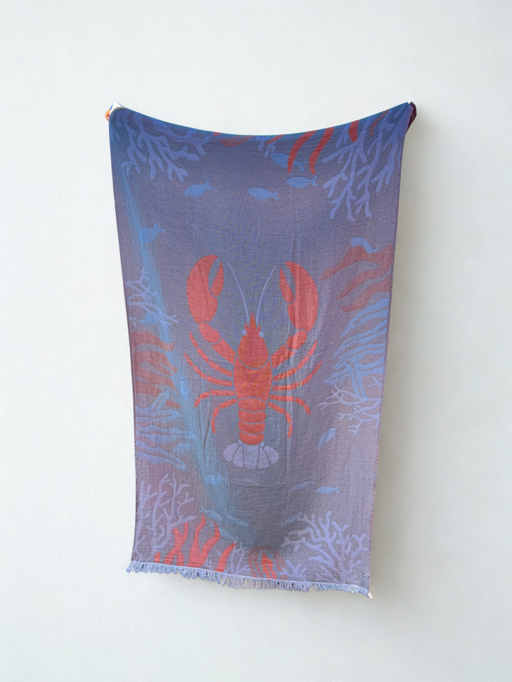 The Lobster Turkish Towel – Quick Drying Beach Towel from turkanhome.com features a bold red lobster with blue and purple coral and fish patterns, displayed against a plain white wall.