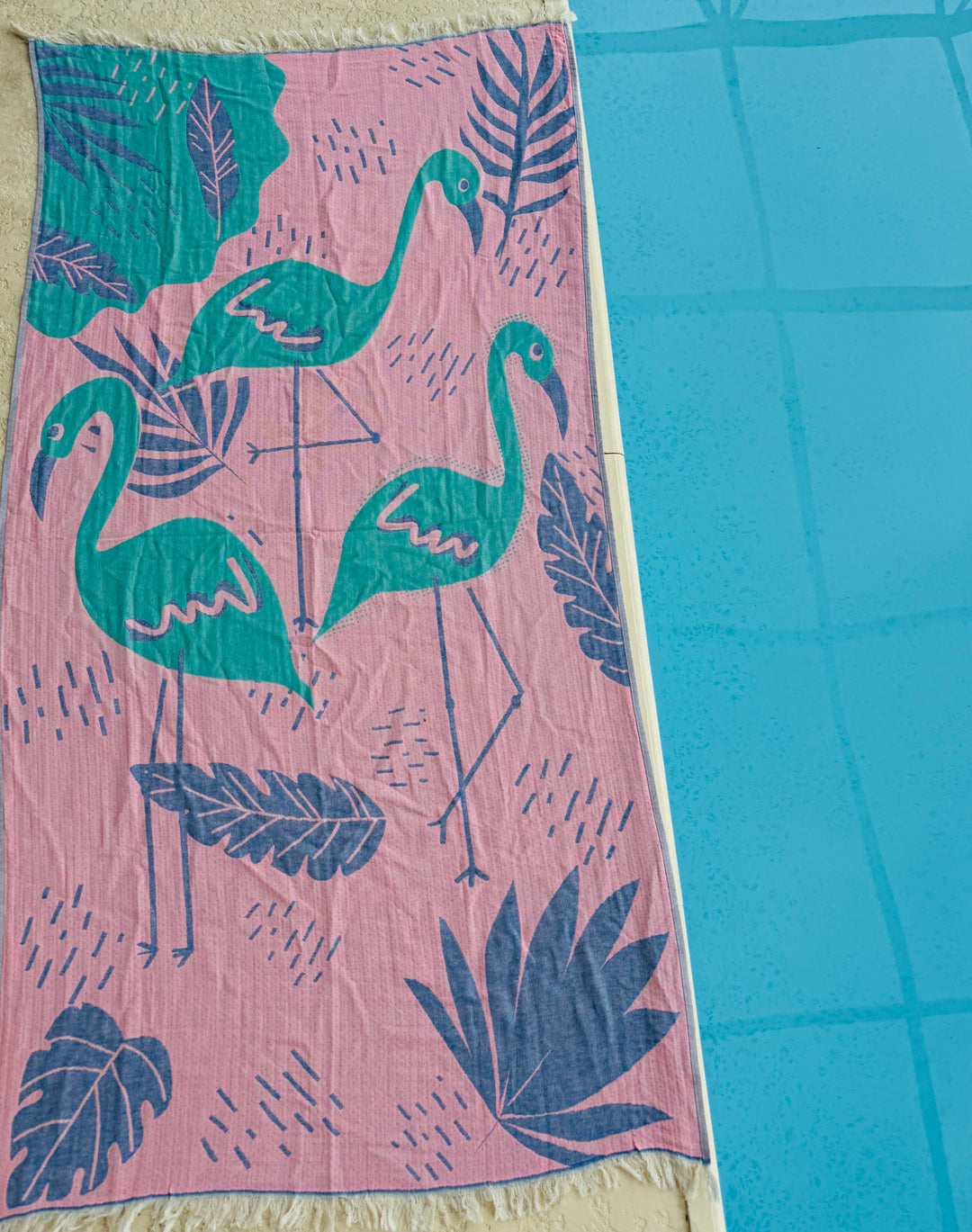The Flamingo Vibe Towel by turkanhome.com is a quick-drying, 100% cotton beach towel with green flamingos and large leaves on a pink background—perfect for poolside relaxation.