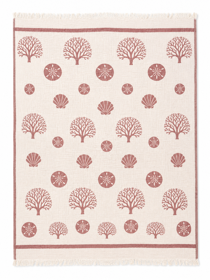 The Coastal Muslin Throw Blanket – Reversible Turkish Cotton from turkanhome.com is a rectangular beige coastal throw adorned with neat rows of red coral, seashell, and sand dollar patterns, framed by coordinating coral motifs and finished with fringe on the short edges.