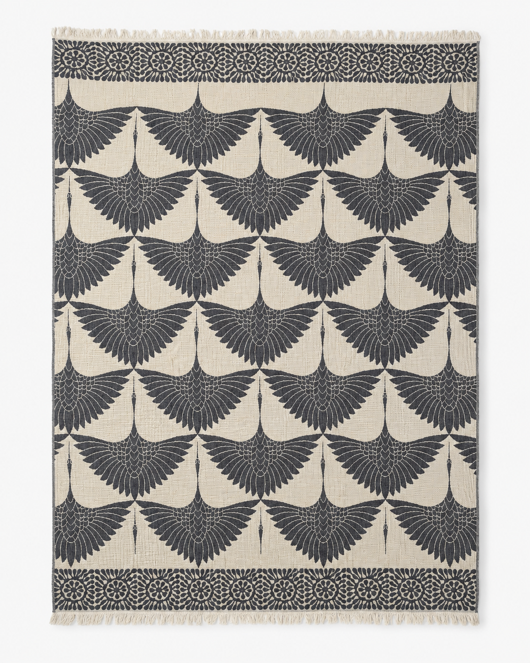 Rewritten Sentence: The Crane Muslin Throw Blanket Natural Border by turkanhome.com is a rectangular, reversible Turkish cotton throw featuring a distinctive crane motif with repeating stylized black birds in flight on a cream background. Decorative black borders adorned with circular and floral accents along the top and bottom edges evoke traditional Turkish artistry.