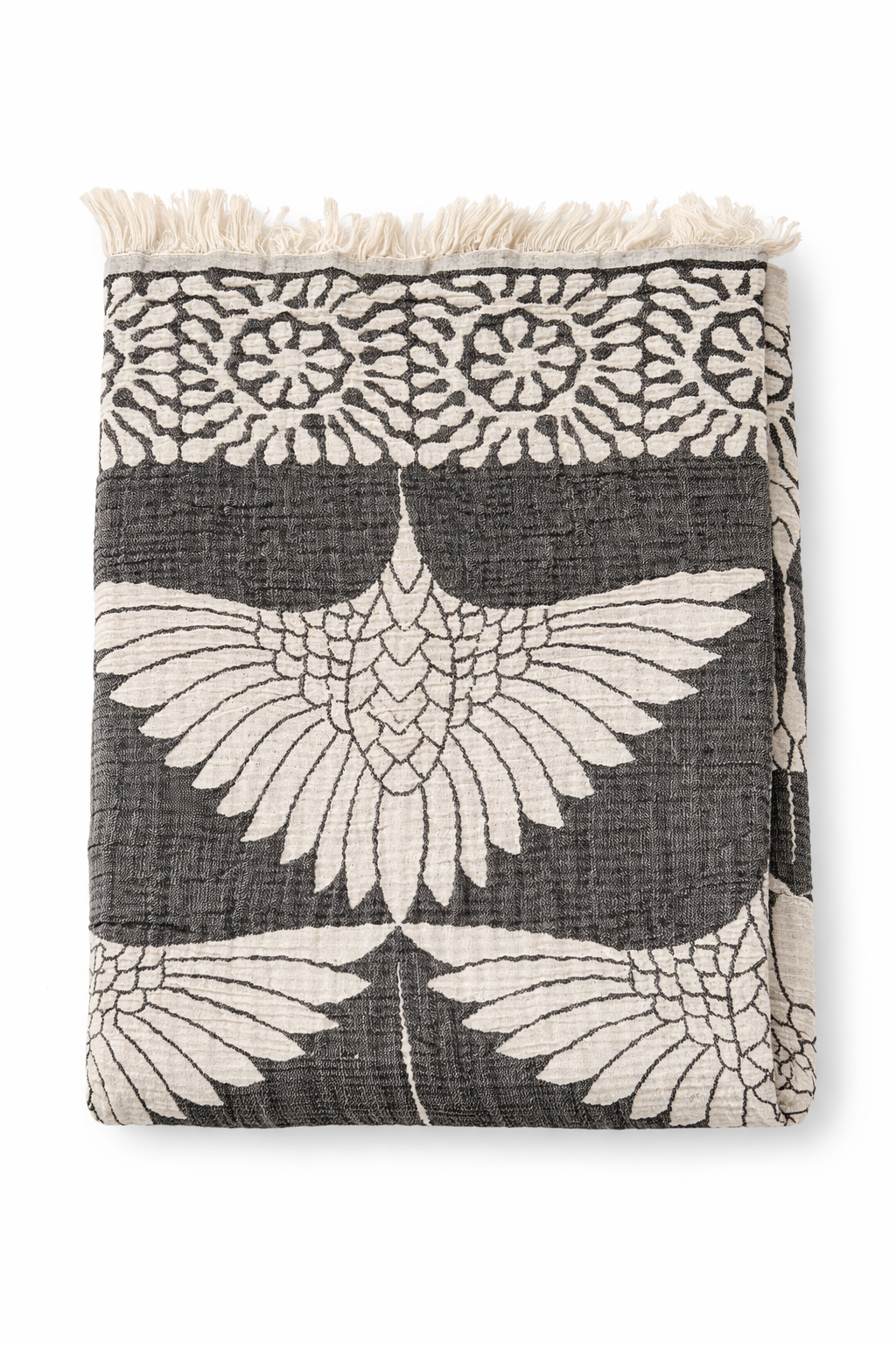 A folded black Crane Muslin Throw Blanket – Reversible Turkish Cotton by turkanhome.com features a white bird and floral pattern with a fringe border.
