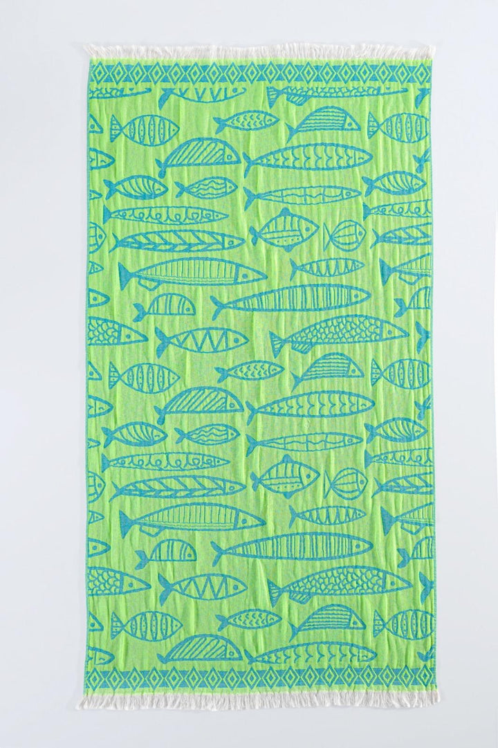 The Fishes Turkish Towel by turkanhome.com is a green rectangular jacquard-woven 100% cotton towel with blue fish and geometric patterns, plus white fringe on the short edges for a soft, durable finish.