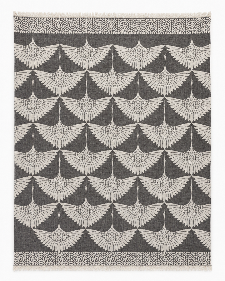 Experience the refined elegance of turkanhome.com's Crane Muslin Throw Blanket Natural Border–Reversible Turkish Cotton, featuring a sophisticated square design with a soft gray backdrop and a repeating white geometric pattern inspired by classic crane motifs, reminiscent of outstretched bird wings. Its border is adorned with circular floral accents, echoing the luxurious detail found in traditional Turkish cotton blankets.