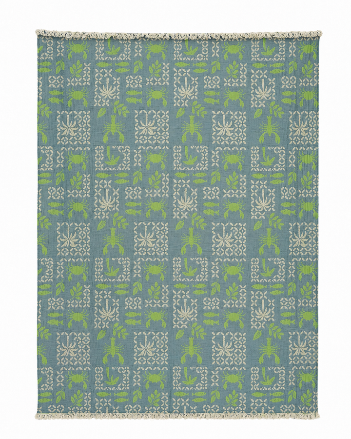The Sea Life Muslin Throw Blanket – Reversible Turkish Cotton from turkanhome.com is a rectangular blue textile adorned with a symmetrical, all-over geometric pattern featuring white and green plants, animals, and shapes. Crafted from soft Turkish cotton, this elegant throw is finished with short white fringe along the edges, making it a stylish addition to any coastal-inspired décor.