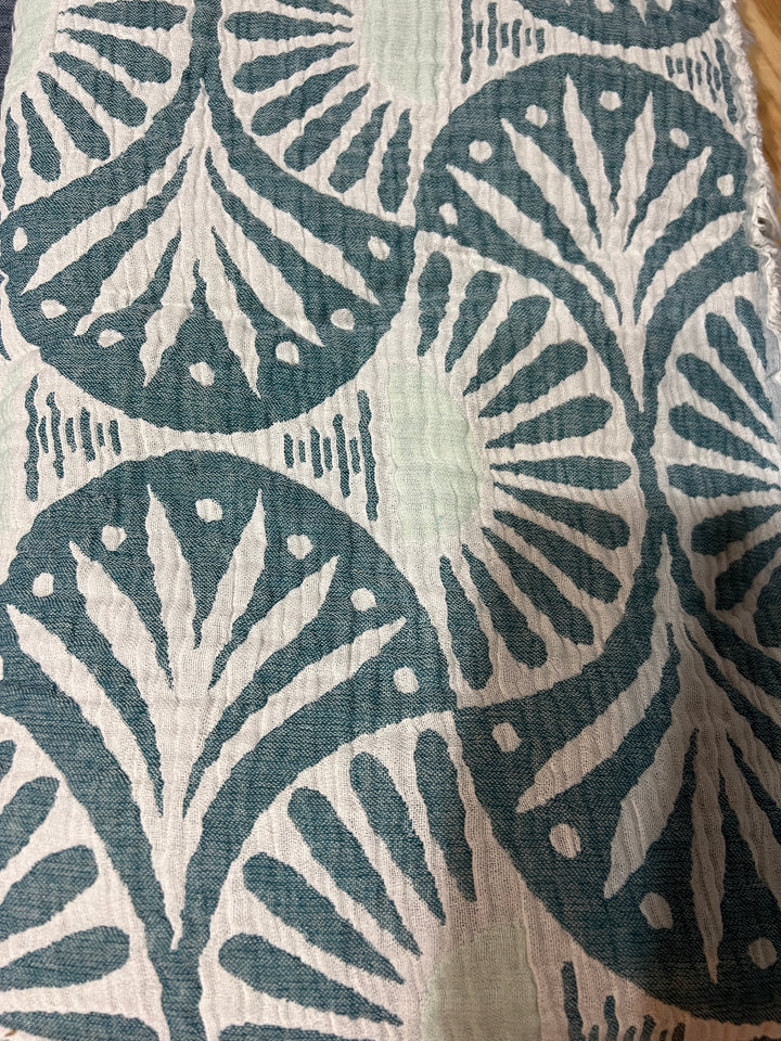 A close-up of the Gingko Muslin Bed Blanket – Teal (King) from turkanhome.com shows softly crinkled, breathable fabric with repeating teal and white fan and dot motifs, evoking the luxury of Turkish cotton.