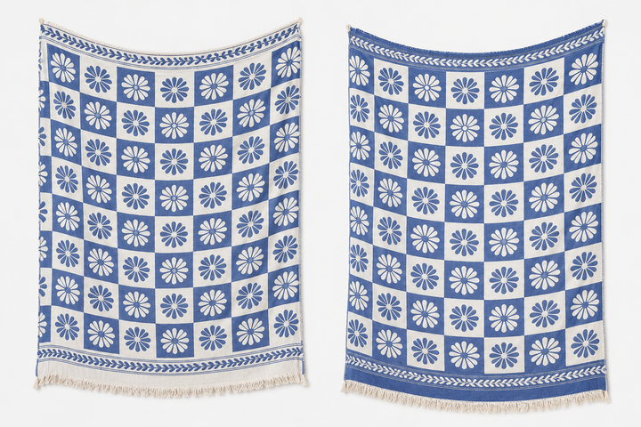 Two Daisy Muslin Throw Blankets from turkanhome.com, made of Turkish cotton, hang side by side. Each features a blue and white square pattern with daisy motifs, decorative top and bottom borders, and fringed edges.
