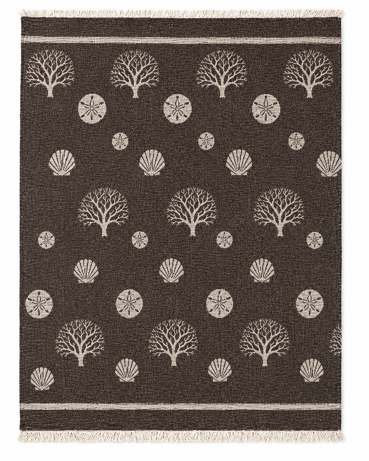 The Coastal Muslin Throw Blanket – Reversible Turkish Cotton from turkanhome.com features a dark brown rectangular design adorned with beige tree, shell, and sand dollar patterns arranged in rows. Reminiscent of a coastal rug, it is finished with short fringe on two ends and two parallel beige stripes near the edges.
