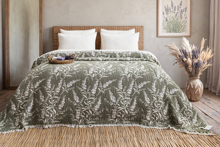 7-Layer Cotton Muslin Quilted Blanket Lavander in sage green with a white floral pattern draped over a bed with white pillows and a woven headboard.