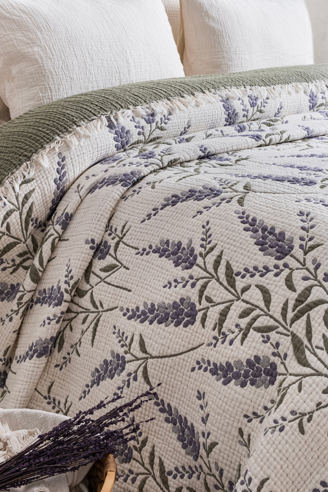 A 7-Layer Cotton Muslin Quilted Blanket Lavander layered over a solid green blanket on a bed.