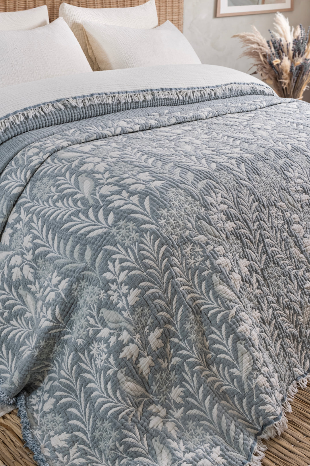 A Luxury 7-Layer Cotton Muslin Quilted Blanket - Mint Bird in light blue cotton muslin with a repeating white botanical pattern draped over a bed as an all-season bedspread.