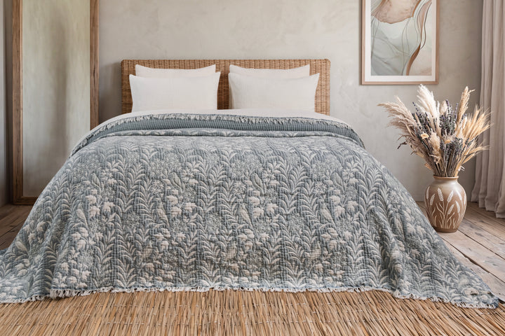 A mint green Luxury 7-Layer Cotton Muslin Quilted Blanket - Mint Bird featuring a botanical bird and leaf pattern draped over a bed.