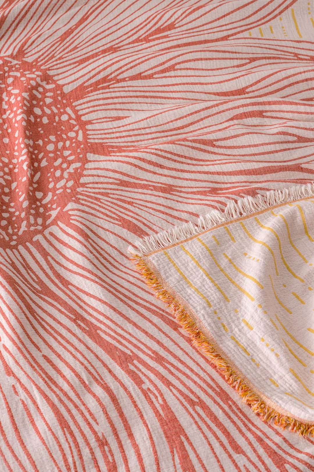 A close-up of the Sunflower Bedspread in Yellow-Brick by turkanhome.com, showing its pink and orange sunburst jacquard pattern with radiating lines, fringed corner, and yellow accents on the underside.
