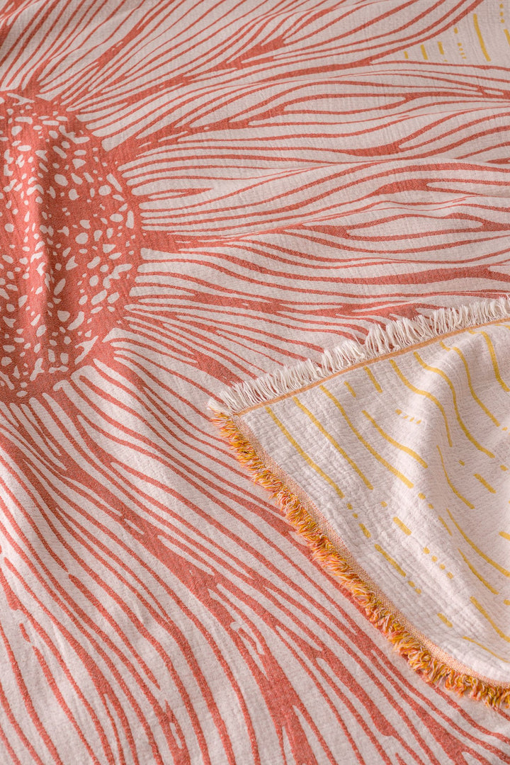 A close-up of the Sunflower Bedspread in Yellow-Brick by turkanhome.com, showing its pink and orange sunburst jacquard pattern with radiating lines, fringed corner, and yellow accents on the underside.