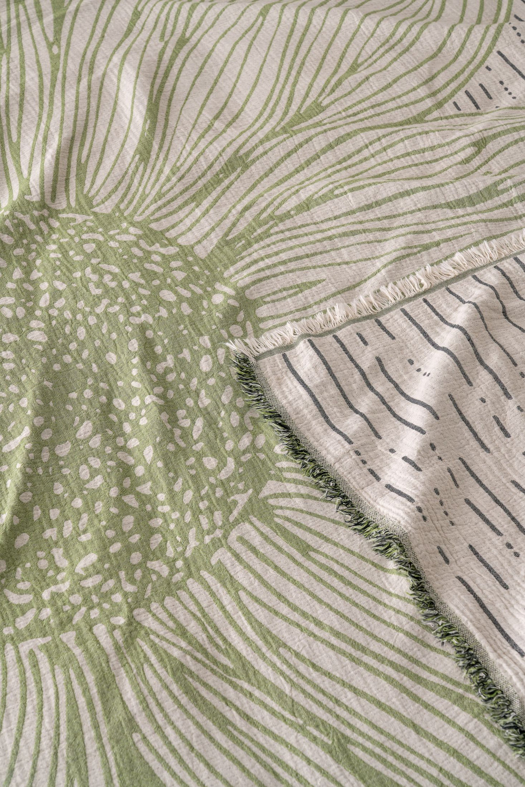 A close-up of the Sunflower Bedspread / Green from turkanhome.com shows its woven jacquard fabric with bold abstract green and white floral patterns, radiating lines, dotted textures, and a slightly folded fringed edge.
