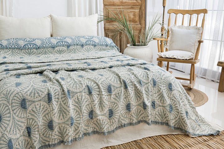 A bed with pillows, a chair, and the Gingko Muslin Bed Blanket – Teal (King-Oversized Queen) from turkanhome.com for added comfort.