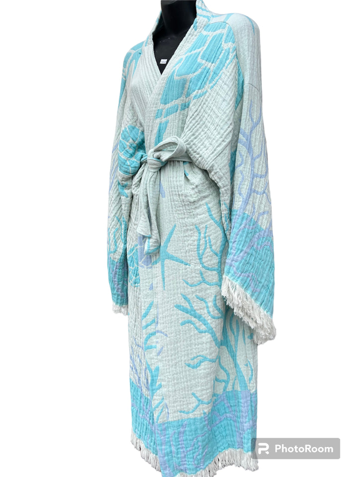 The Blue Turtle Robe by turkanhome.com is a light blue and white kimono with a sea-inspired pattern, sash belt, wide sleeves, and fringe trim—ideal as elegant beach or lounge wear. Displayed on a black mannequin against a white background.